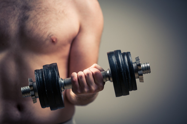 Close up of young man lifting weights over grey background - Foto, Bild