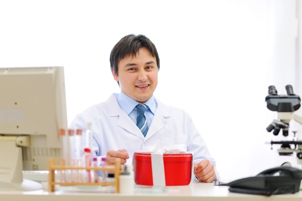 Happy medical doctor sitting at table with present box - 写真・画像