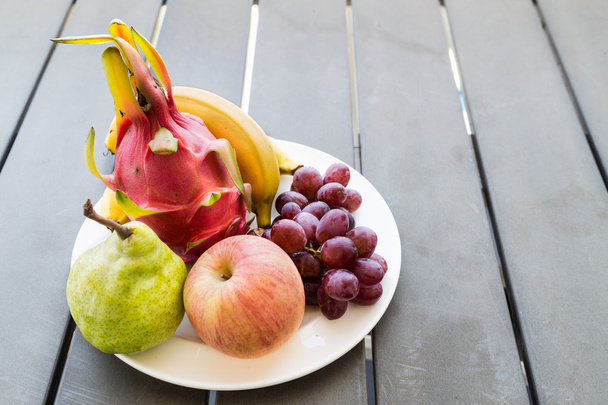 Свежие фрукты на тарелке, подаваемые на деревянном столе
 - Фото, изображение