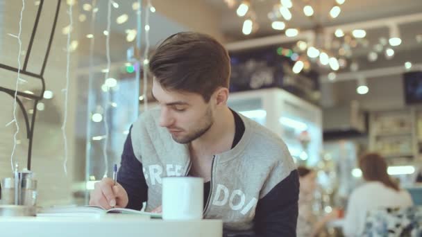 Young man writing in notepad in cafe - 映像、動画