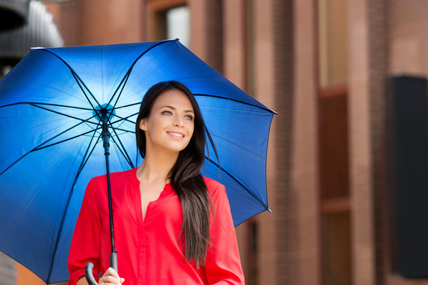 Attractive young woman in red shirt posing with blue umbrella - Fotó, kép
