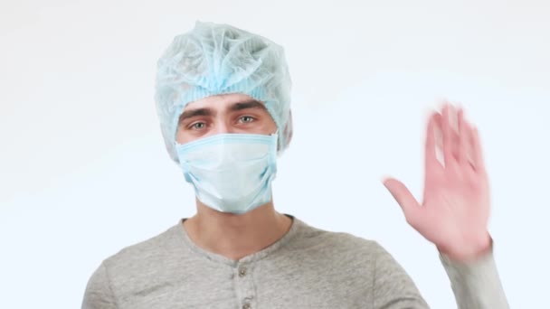若い医師を振って、見て身に着けているマスクおよび医療キャップ、Camera.A 男。白い背景の上に男が立っています。. - 映像、動画
