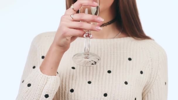 Beautiful girl drinking wine from a glass and lovely smiles. A girl standing on a white background. New Year - Imágenes, Vídeo