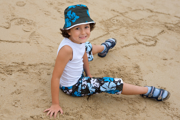 Гарненький хлопчик сидить на піску з пляжу
 - Фото, зображення