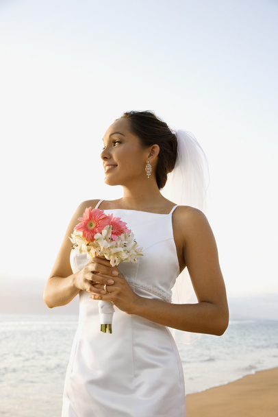 Bride holding bouquet on beach. - 写真・画像