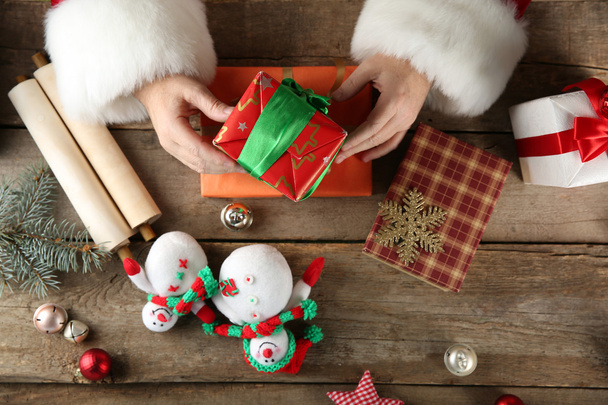 Beautiful gift box in Santa Claus's hands and Christmas decorations on wooden table, close up - Foto, afbeelding