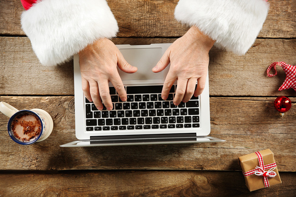 Santa hands typing on laptop on wooden table, close up - Фото, изображение