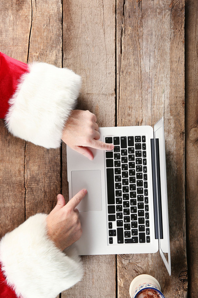 Santa hands typing on laptop on wooden table, close up - Foto, Imagem