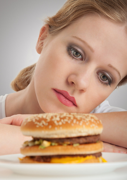 Hermosa chica se sienta en una dieta, triste al mirar una hamburguesa
 - Foto, Imagen