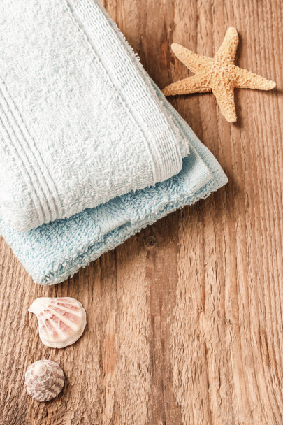Towels, shells and a starfish on wooden table - Фото, изображение