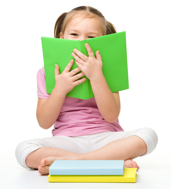 Cute little girl is hiding behind a book - Fotoğraf, Görsel