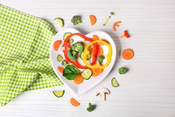 Полезные нарезанные овощи на тарелке в виде сердца на деревянном столе вид сверху
 - Фото, изображение
