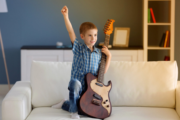 Little boy with a guitar on a sofa - Zdjęcie, obraz
