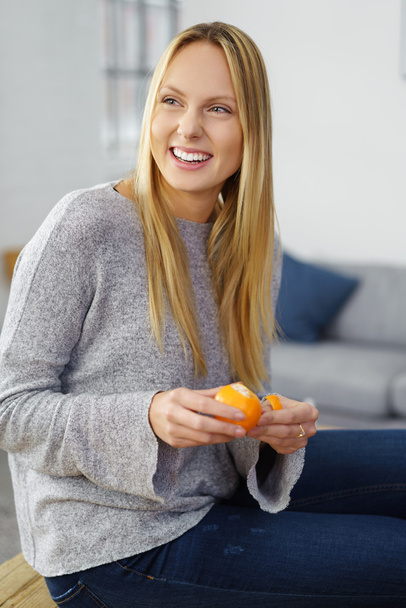 Χαμογελώντας ευτυχισμένη γυναίκα που καθαρίζει ένα πορτοκάλι - Φωτογραφία, εικόνα
