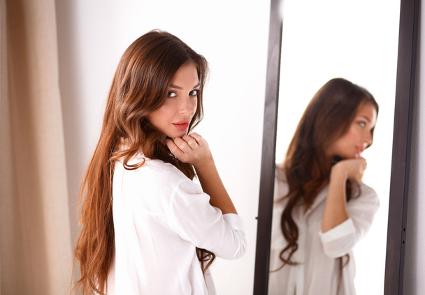 Young woman looking herself reflection in mirror at home - 写真・画像