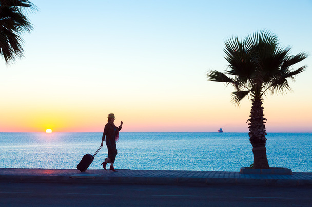 Exotische Urlaubs-Silhouette einer Frau, die einen Reisekoffer am Meer zieht - Foto, Bild