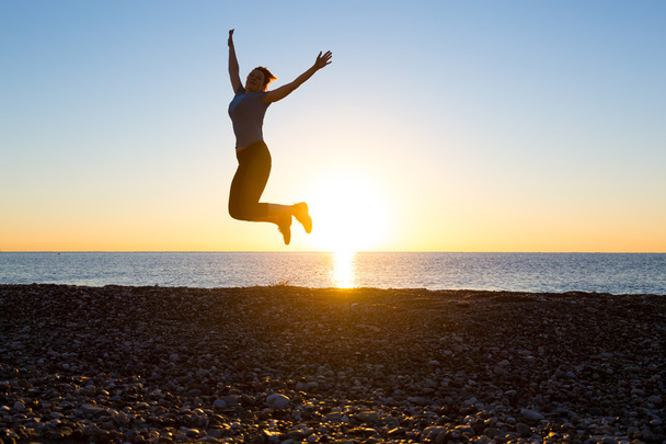 Silhueta de Happy Female pulando alto com os braços levantados na praia nascer do sol
 - Foto, Imagem
