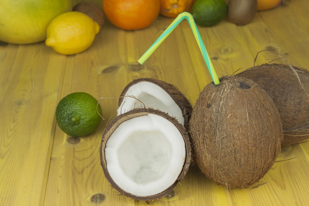 Gebarsten kokosnoot op gele houten tafel. Voorbereiding van kokosnoot verfrissend drankje. Tropisch drankje. De tabel in de strandbar. Een verfrissende drank gemaakt van kokosmelk. - Foto, afbeelding