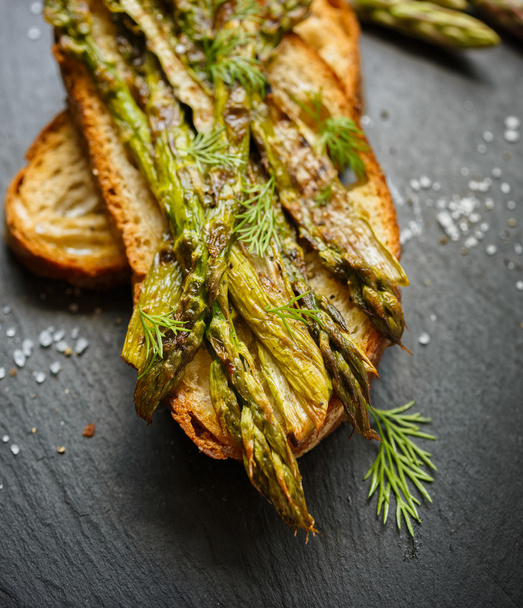 Grilled country bread with grilled green asparagus on a dark background - Photo, Image