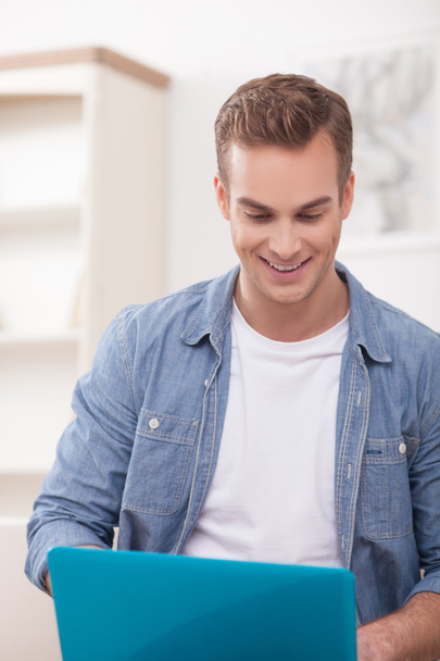 Cheerful guy is using a notebook at home - Photo, image