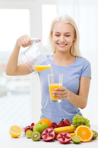 smiling woman pouring fruit juice to glass at home - Foto, Bild
