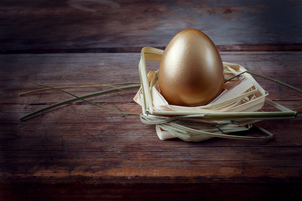 Golden egg on wooden table in  straw nest - Photo, Image