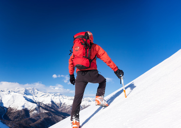 El escalador sube por una ladera nevada. Temporada de invierno, cielo despejado
. - Foto, imagen