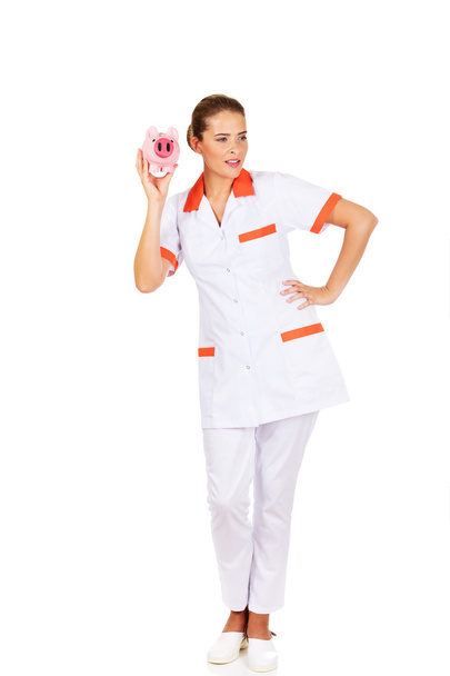 Young beautiful female doctor or nurse holding a piggybank - Fotoğraf, Görsel