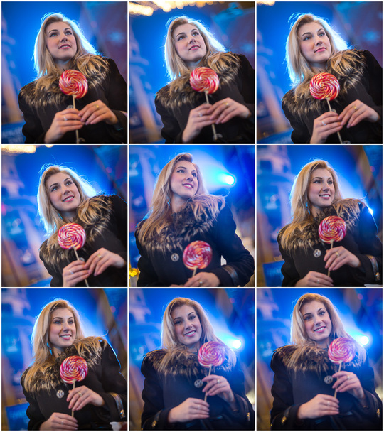 Portrait of young woman with long fair hair posing outdoor in cold winter evening. Beautiful blonde holding a big lollipop with Xmas lights on background. Attractive female smiling in Xmas market - Fotoğraf, Görsel