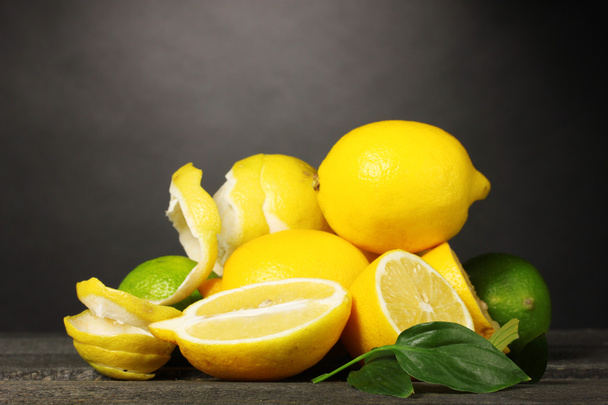 Ripe lemons and limes with leaves on wooden table on grey background - Foto, Imagem