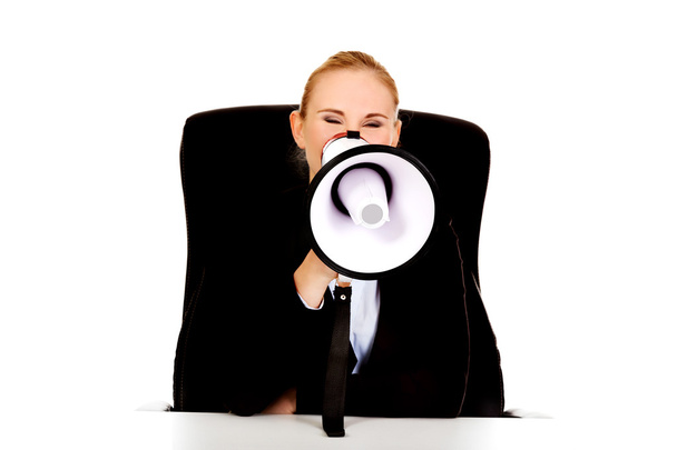 Business woman sitting behind the desk and screaming through a megaphone - Foto, Bild