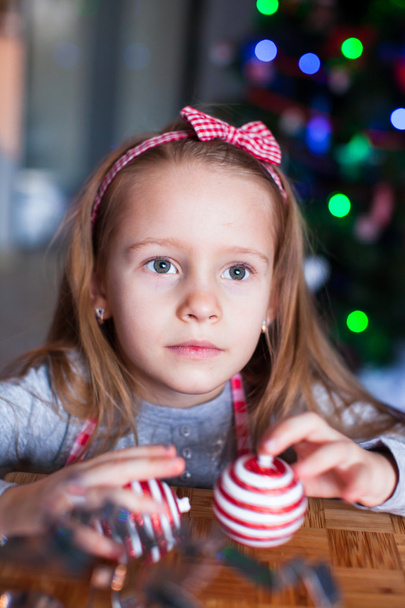 Adorable dziewczyna pieczenia ciasteczka świąteczne na Boże Narodzenie. Choinka i światła na tle. - Zdjęcie, obraz
