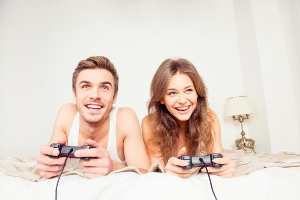 Happy couple in love playing video games with joysticks on the b - Φωτογραφία, εικόνα