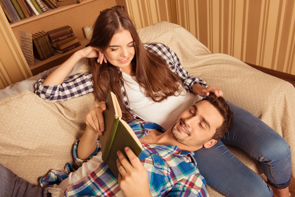 Beautiful girl holding her boyfriend's head on her knees reading - Photo, image