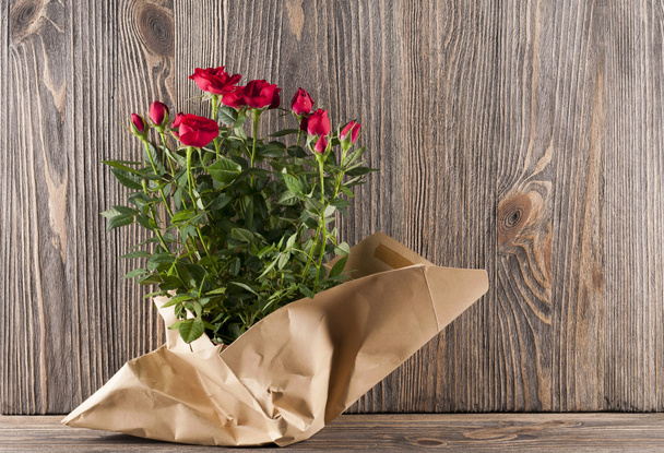 Red rose flowers in paper-bag on a wooden background - Фото, изображение