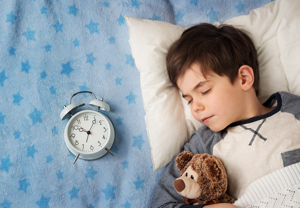 six years old child sleeping in bed with alarm clock - Foto, afbeelding