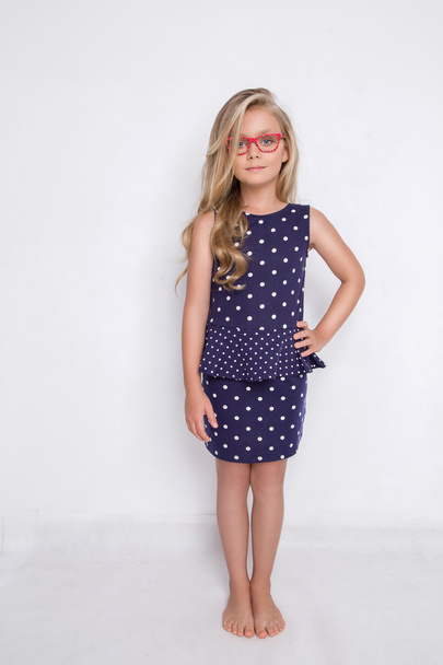 Portrait of a lovely little girl daughter in long blond hair and violet, blue dress with white dots and red glasses with white dots looks at the camera, photo on the white background amazing eyes - Foto, Bild