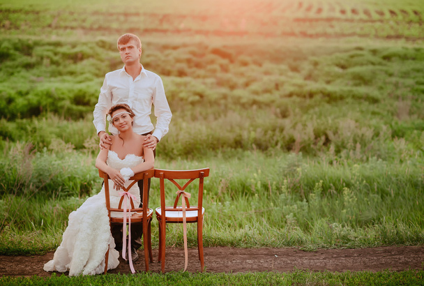 Beautiful young bride and groom sitting chairs in the sunset light - Photo, image