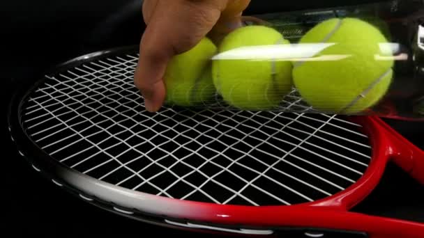Χέρι, βάζοντας το σύνολο τρία νέα μπάλες του τένις πάνω από την ρακέτα του τένις σε μαύρο φόντο - Πλάνα, βίντεο