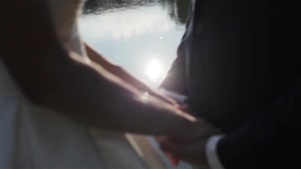 Close-up van jonge paar verliefd houden handen staan in de buurt van het meer in een rug verlicht - Video