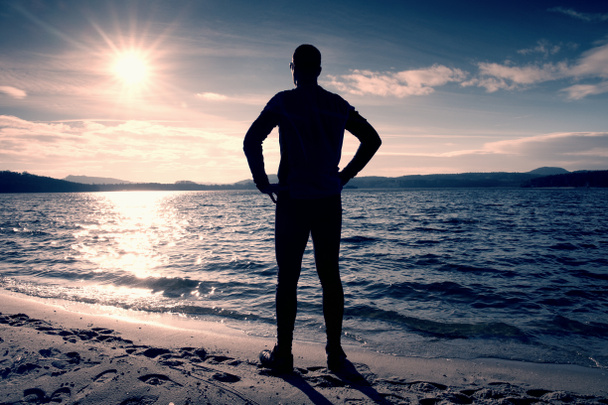 Silhouette di persona in abbigliamento sportivo e capelli corti sulla spiaggia vedi al sole sopra il mare
 - Foto, immagini