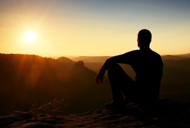 Sportsmann turista v černém oblečení sedí na vrcholu hory a odpočiňte si. Turistické hodinky na ranní zamlžené údolí. - Fotografie, Obrázek