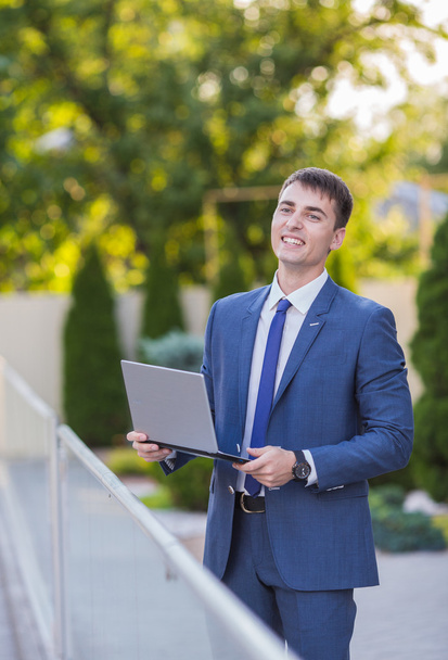 Successful businessman standing in the street holding a laptop - Foto, afbeelding