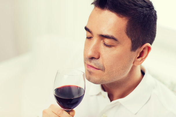 ευτυχισμένος άνθρωπος πόσιμο κόκκινο κρασί από το γυαλί στο σπίτι - Φωτογραφία, εικόνα