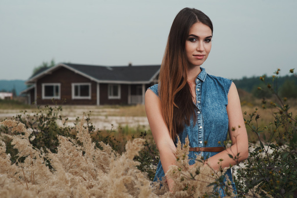 lindo campo señora de pie en la hierba alta contra rancho casa
 - Foto, imagen