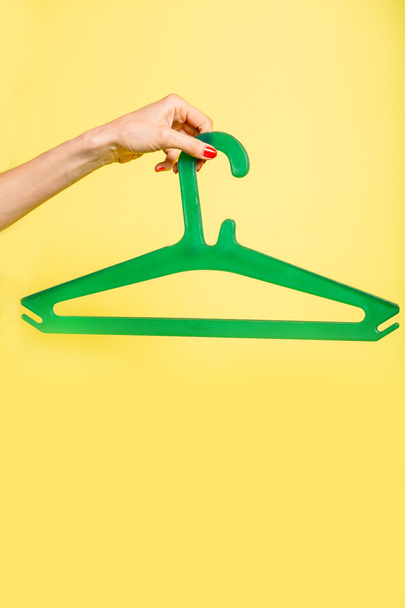 Woman holds green hanger over yellow - Foto, Imagem