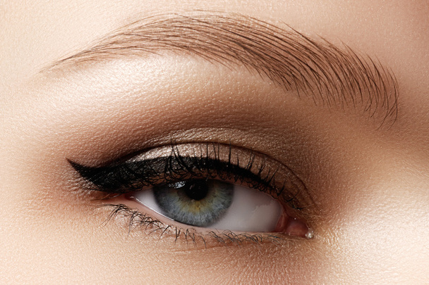 Cosmetics & make-up. Beautiful female eye with sexy black liner makeup. Fashion big arrow shape on woman's eyelid. Chic evening make-up - 写真・画像