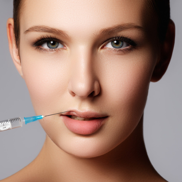 Closeup of beautiful woman gets injection in her lips. Full lips. Beautiful face and the syringe (plastic surgery and cosmetic injection concept). - Zdjęcie, obraz