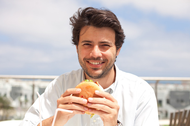 νεαρός άνδρας τρώει ένα χάμπουργκερ - Φωτογραφία, εικόνα