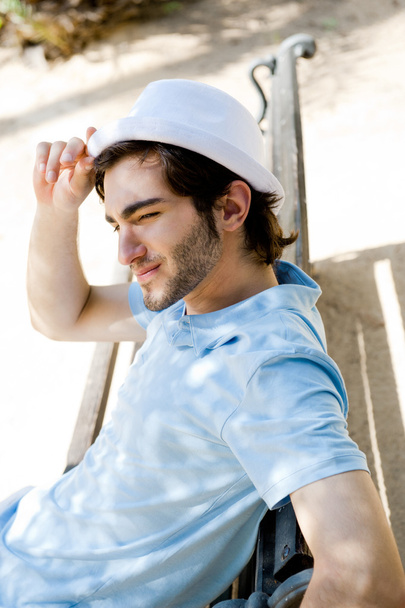 Portrait of a handsome young man sitting in the sun on bench at park - 写真・画像